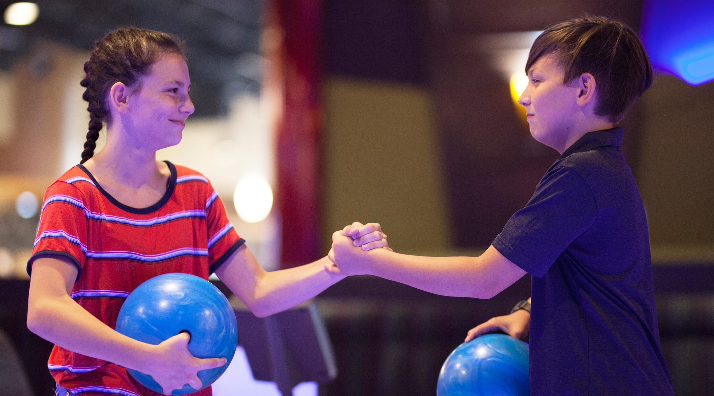 2 Kids shaking hands while each is holding a bowling ball